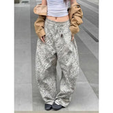 Person wearing leopard print pants and a beige jacket on a gray floor.